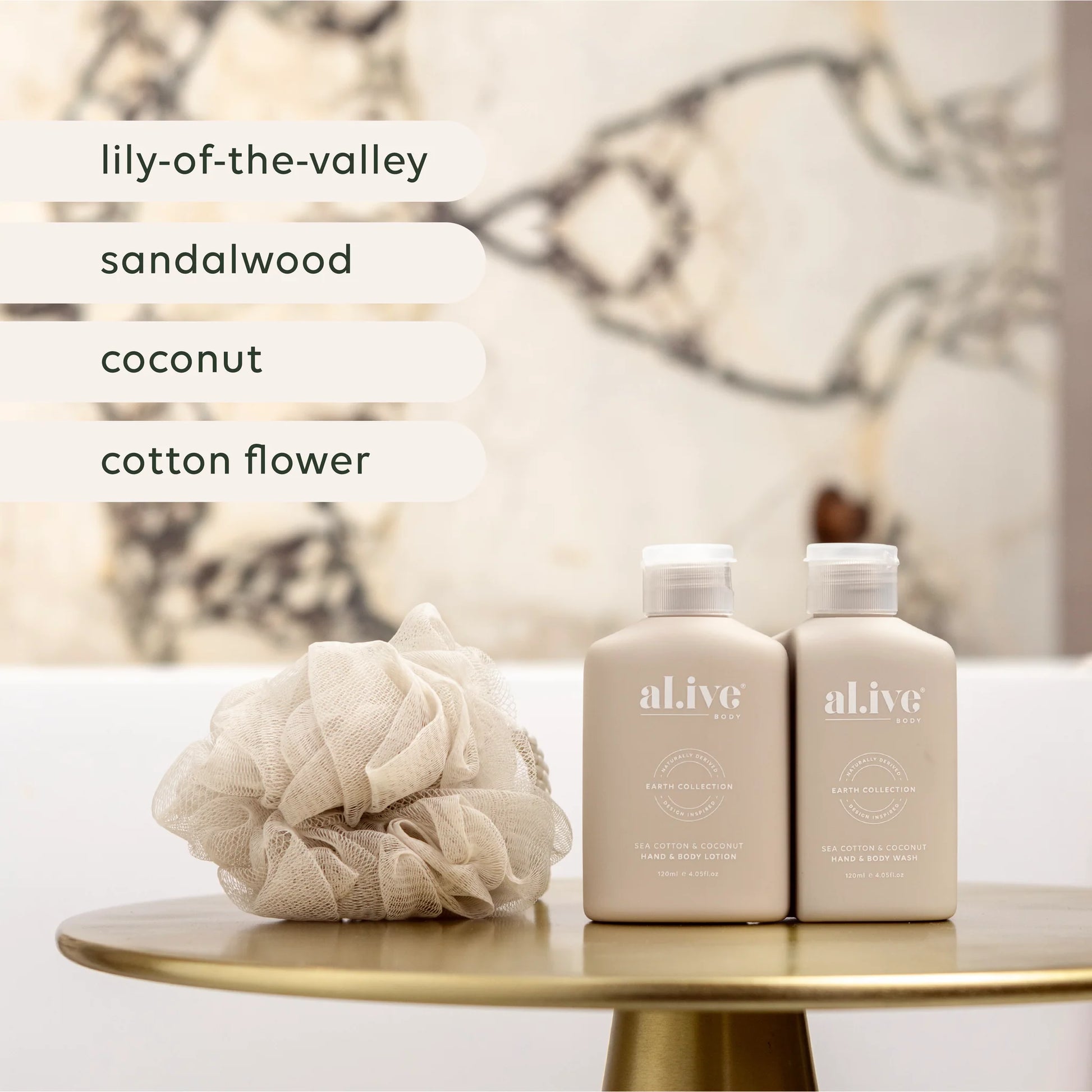 Two bottles of 'alive' products on a table with a loofah, against a blurred decorative wall.