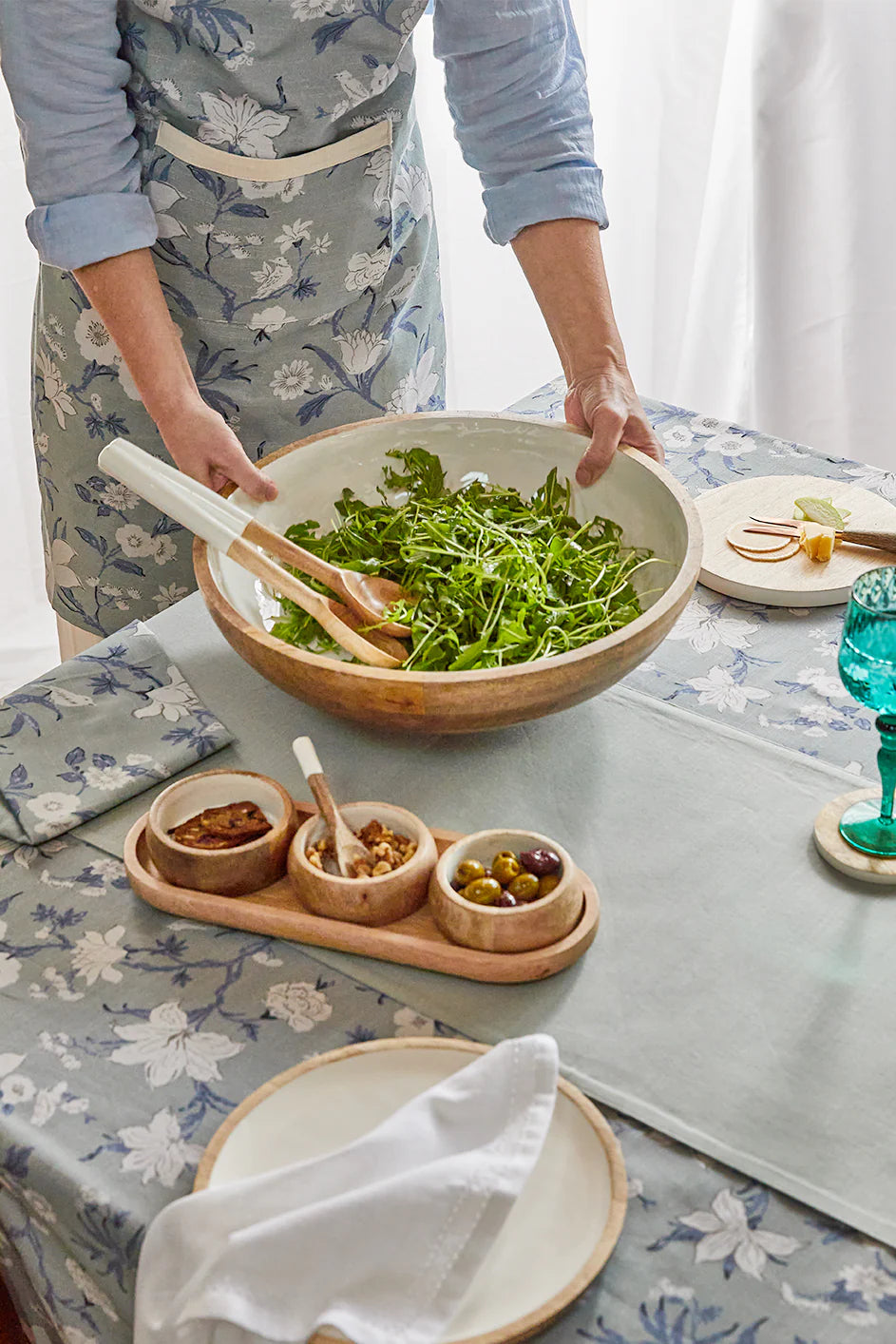Person holding a large bowl of salad on a table with a floral tablecloth.