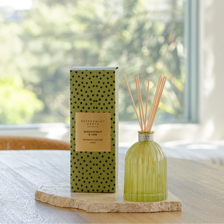 Green diffuser bottle with reeds and packaging on a wooden stand with a blurred green outdoor background