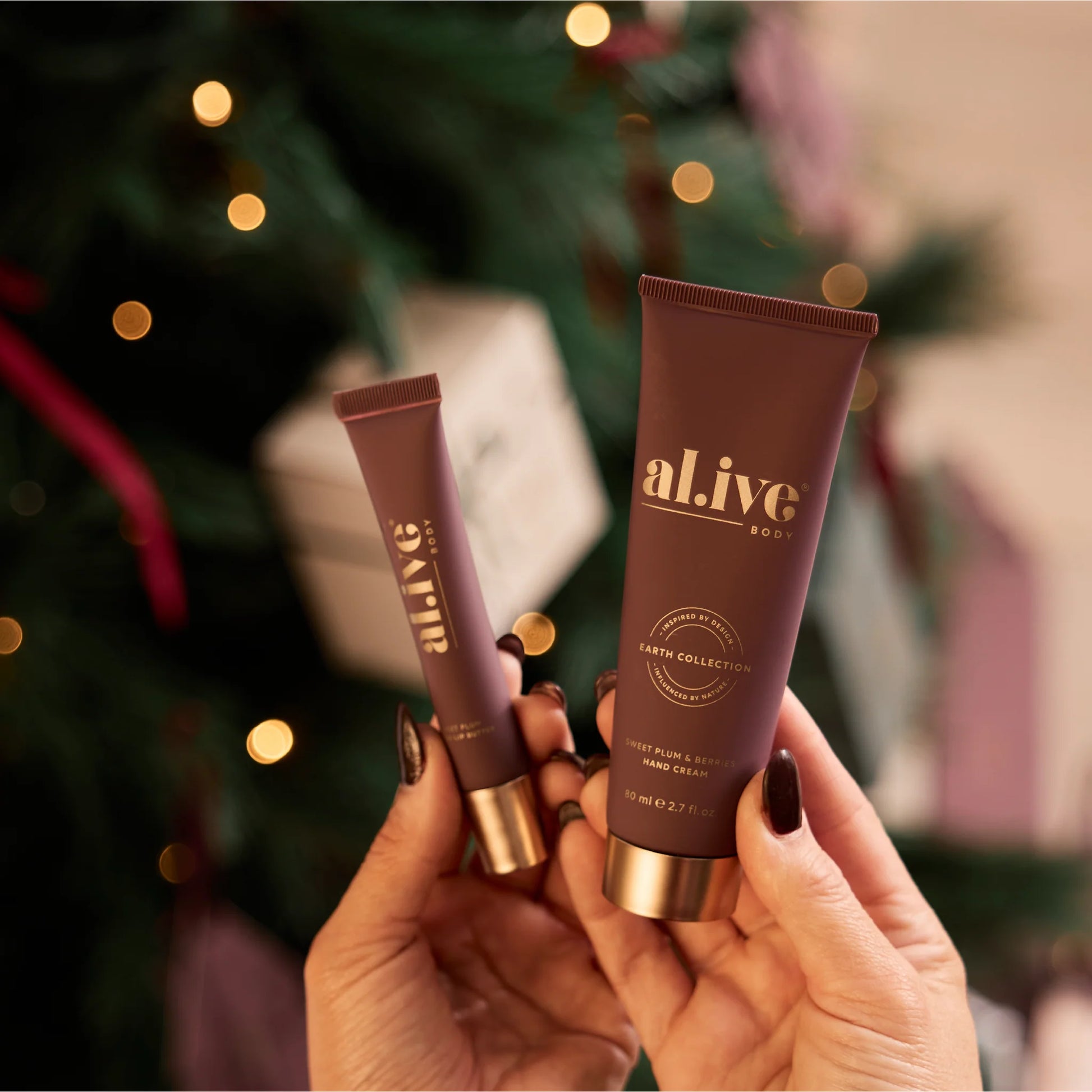 Two 'alive' hand creams held in front of a blurred Christmas tree background