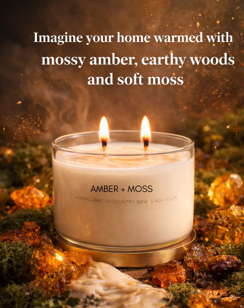 Candle with 'Amber + Moss' branding on a background of moss and amber leaves.