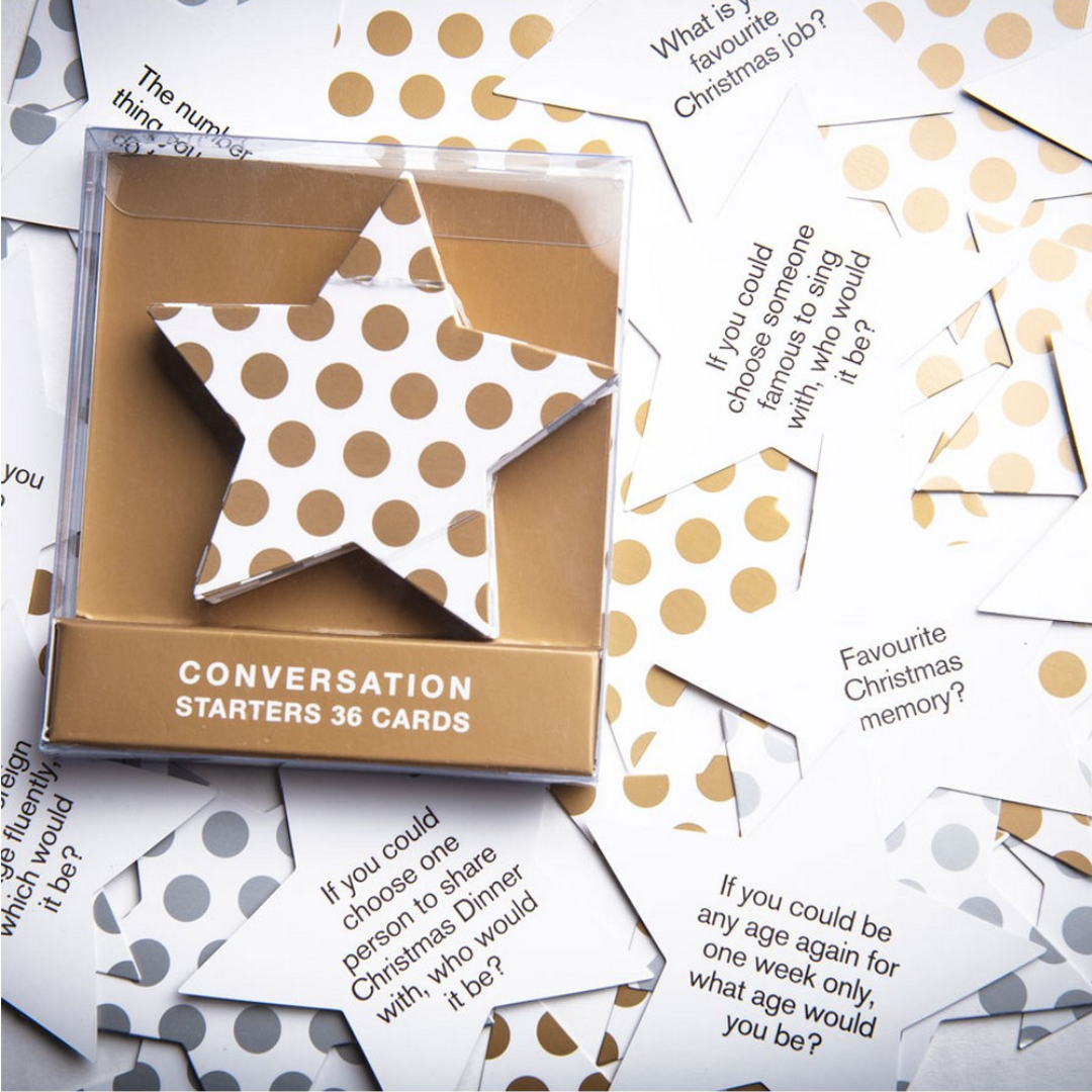 A set of star-shaped conversation starter cards with gold polka dots on a Christmas game packaging, placed on a surface with scattered pieces of the same cards.