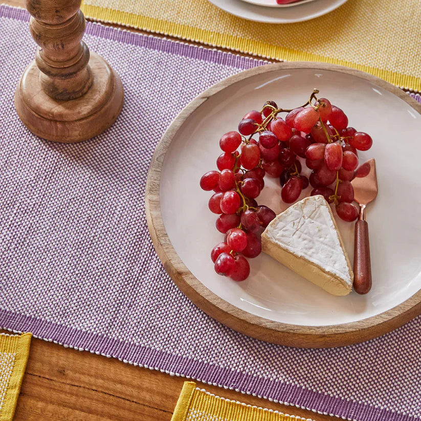 Plate with a slice of cheese and red grapes on a table with a purple placemat.