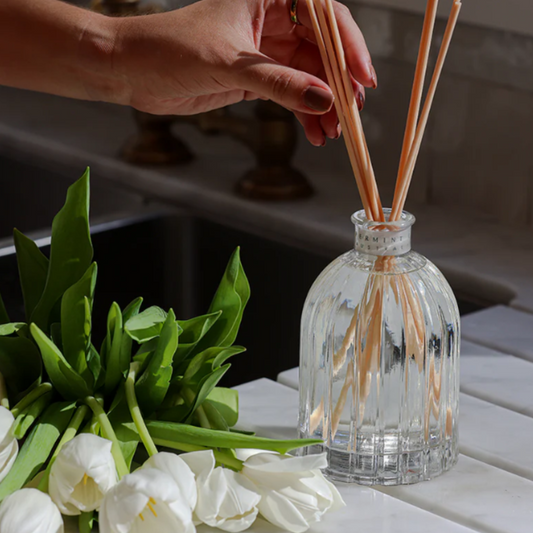 Clear diffuser bottle with reeds and white tulips on a wooden surface