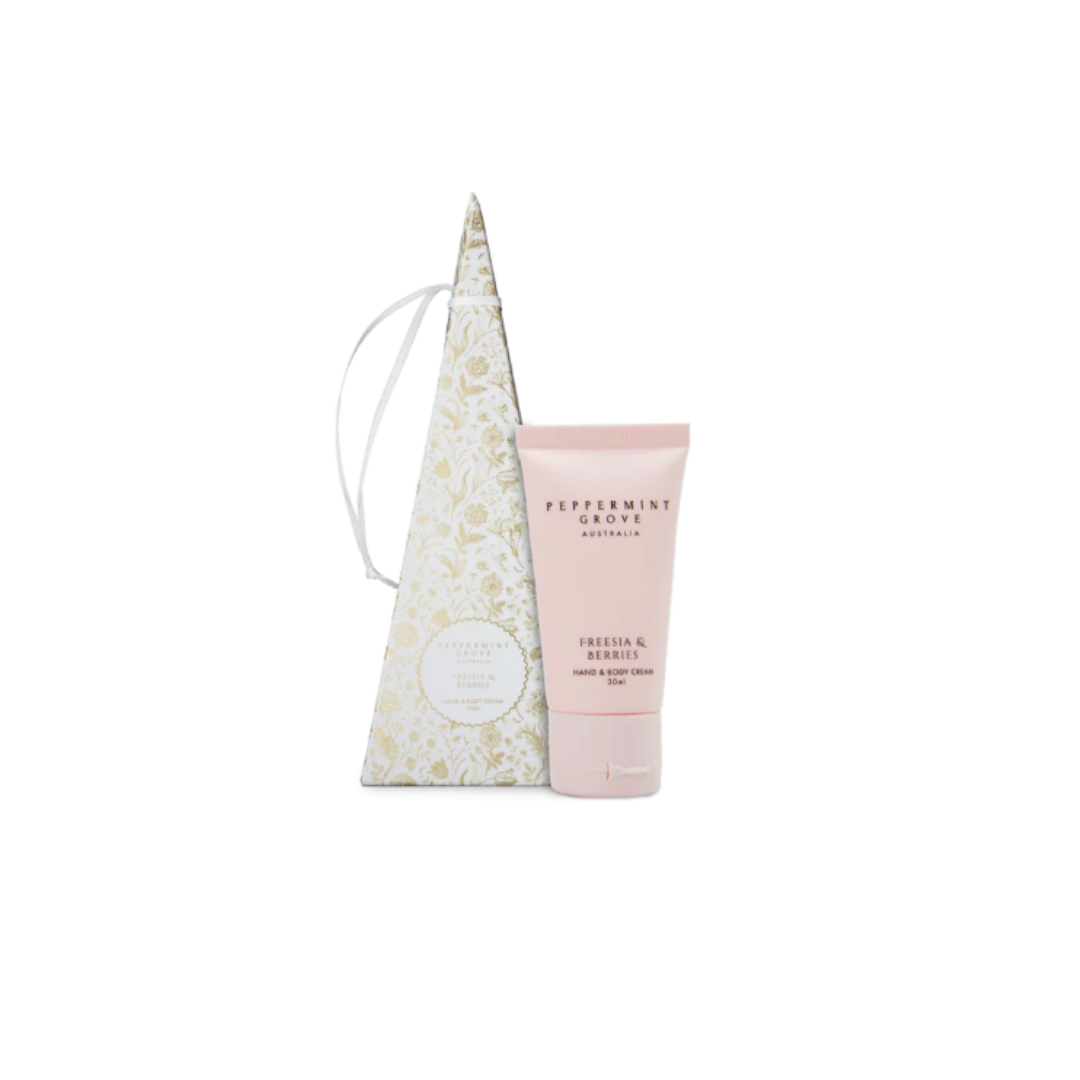 A pink tube of Peppermint Cream hand and body cream stands in front of a tall, pointed cream-colored gift box with a gold floral pattern and a white drawstring, on a plain white background.