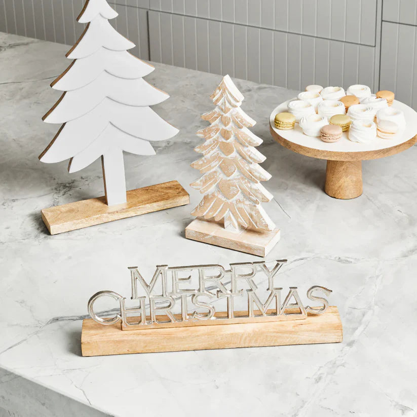 Wooden Christmas decorations including trees and 'Merry Christmas' sign on a light surface.