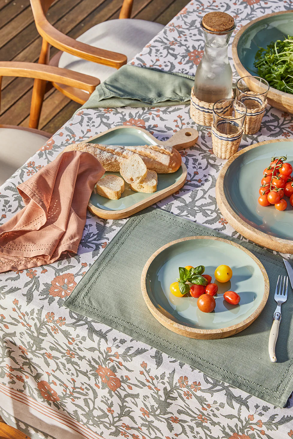 Outdoor dining setup with plates of food, glasses, and a bottle on a patterned tablecloth.