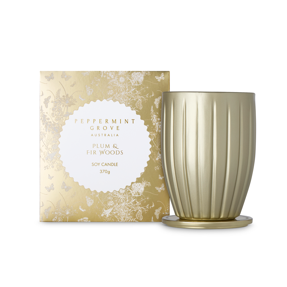 A 370g soy candle in a ribbed metallic gold glass vessel with a matching gold base, shown next to its decorative gold and white floral outer box. The label reads 'PEPPERMINT GROVE AUSTRALIA PLUM & FIR WOODS'.