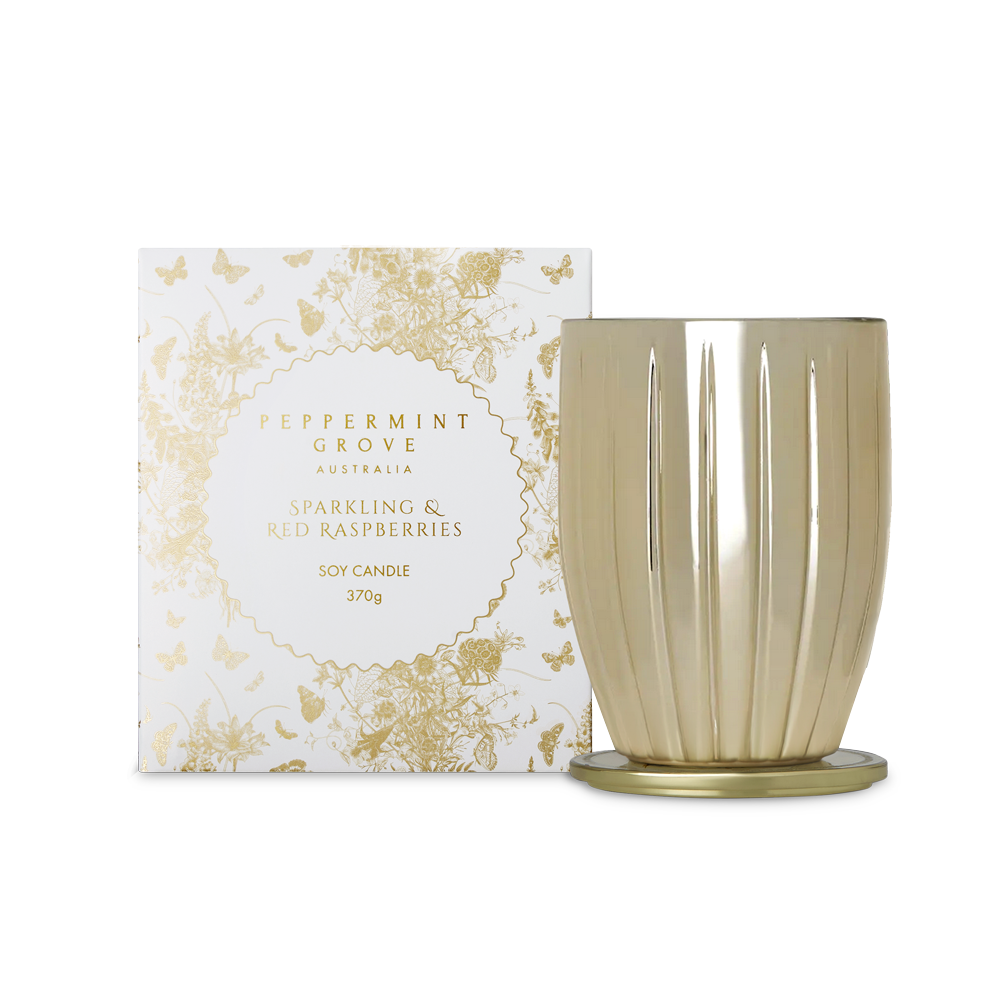 A Peppermint Grove soy candle in a fluted metallic gold glass vessel with a matching gold base, shown next to its white and gold patterned packaging box.