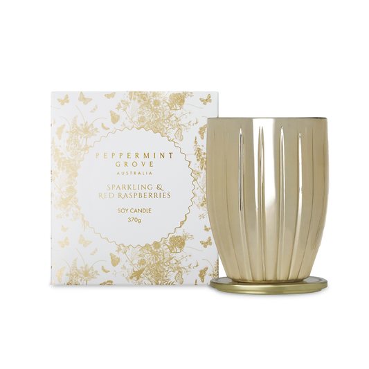 A Peppermint Grove soy candle in a fluted metallic gold glass vessel with a matching gold base, shown next to its white and gold patterned packaging box.
