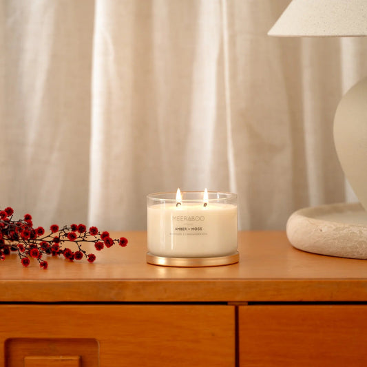 Candle on a wooden surface with a lamp and decorative branches in the background