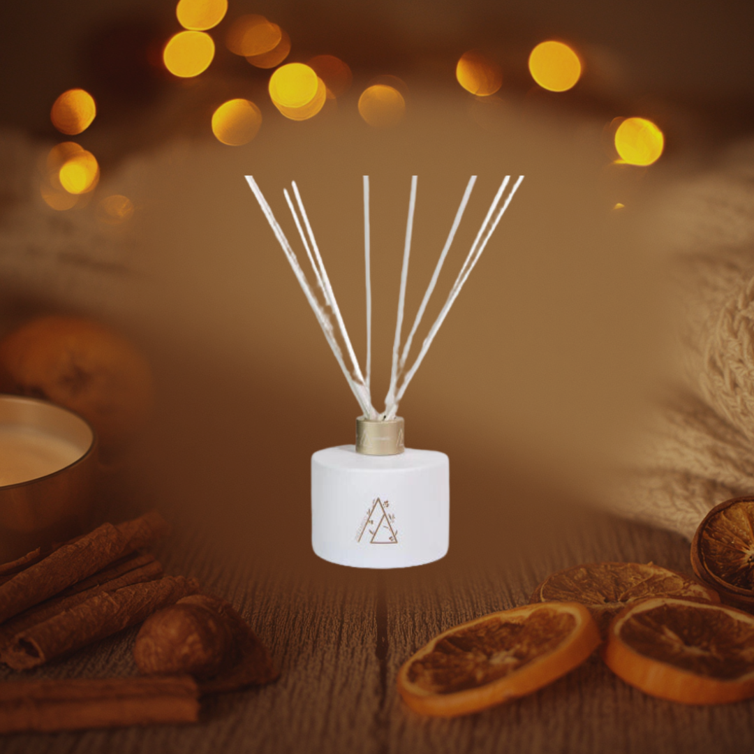 Diffuser with reeds on a wooden surface with cinnamon sticks and oranges, blurred lights in the background