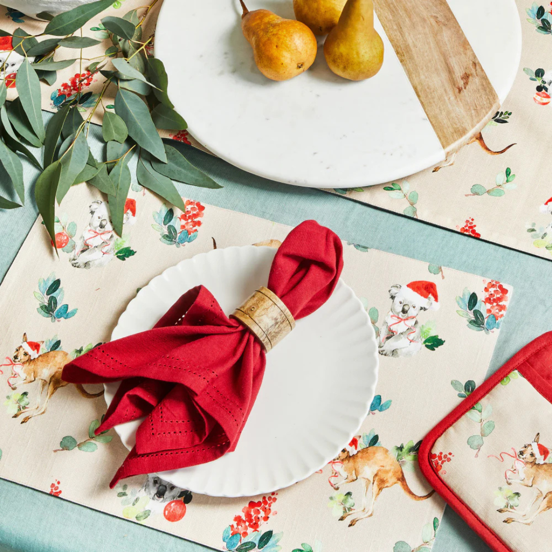Table setting with red napkin, white plate, and floral placemat featuring animal illustrations.